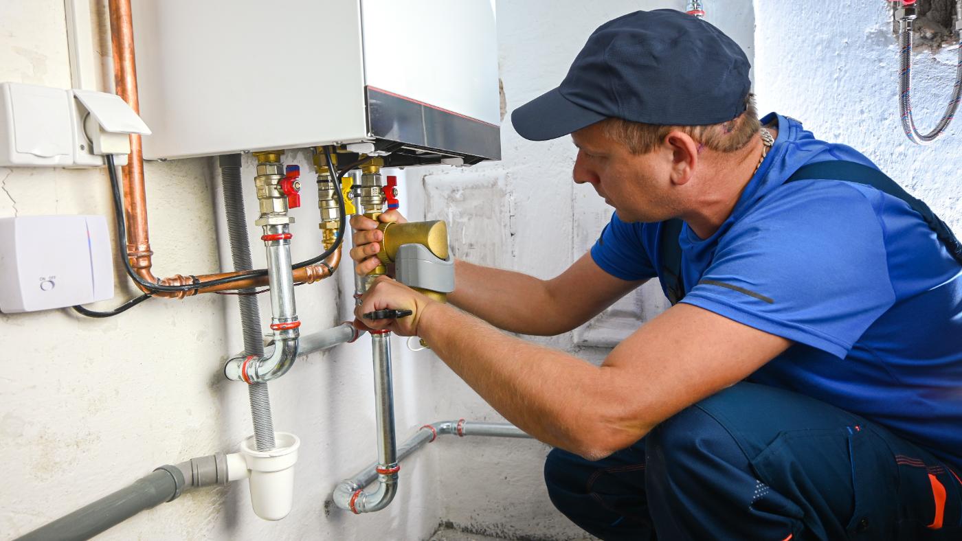 Licensed plumber servicing a wall-mounted tankless water heater and shut-off valves